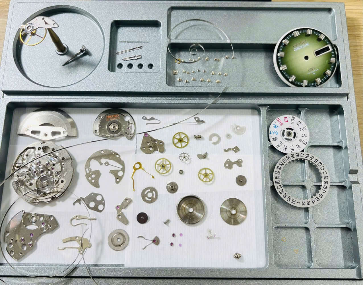 Vintage Seiko 5 Actus 6106-7690 watch parts and movement components on a tray with green dial.