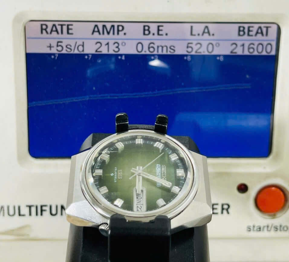 Vintage Seiko 5 Actus 6106-7690 on timing machine, showcasing green dial, with multimeter readings behind.