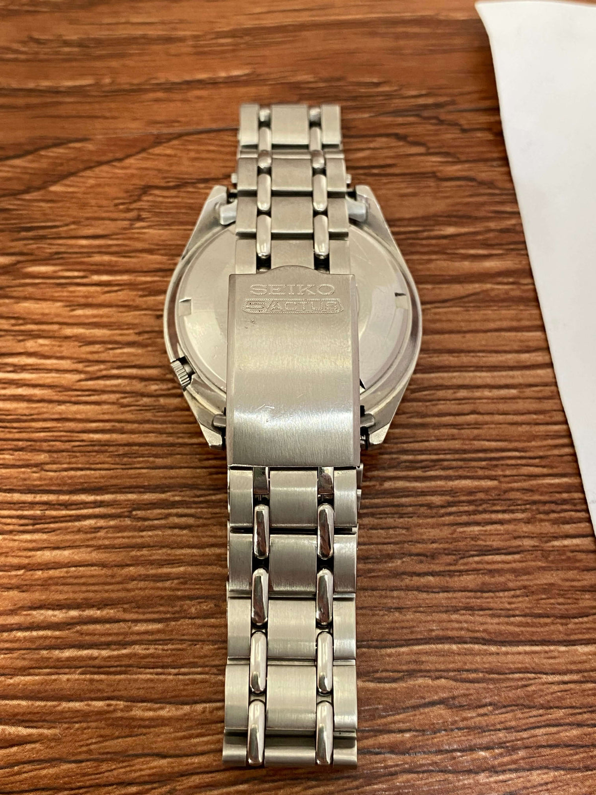 Vintage Seiko 5 SS Actus 6106-7510 case back and stainless steel strap on a wooden surface.