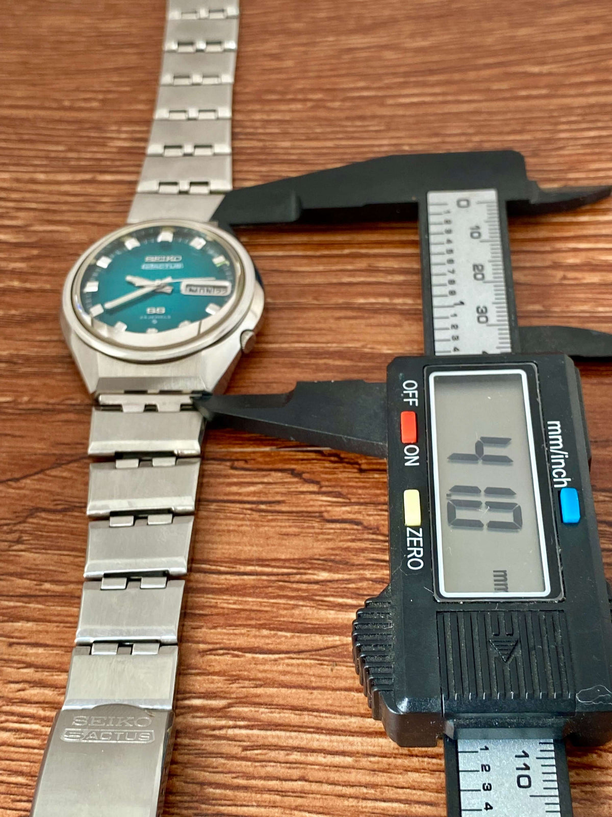 Vintage Seiko 5 Actus 6106-7690 measured next to a digital caliper on wood background with turquoise dial