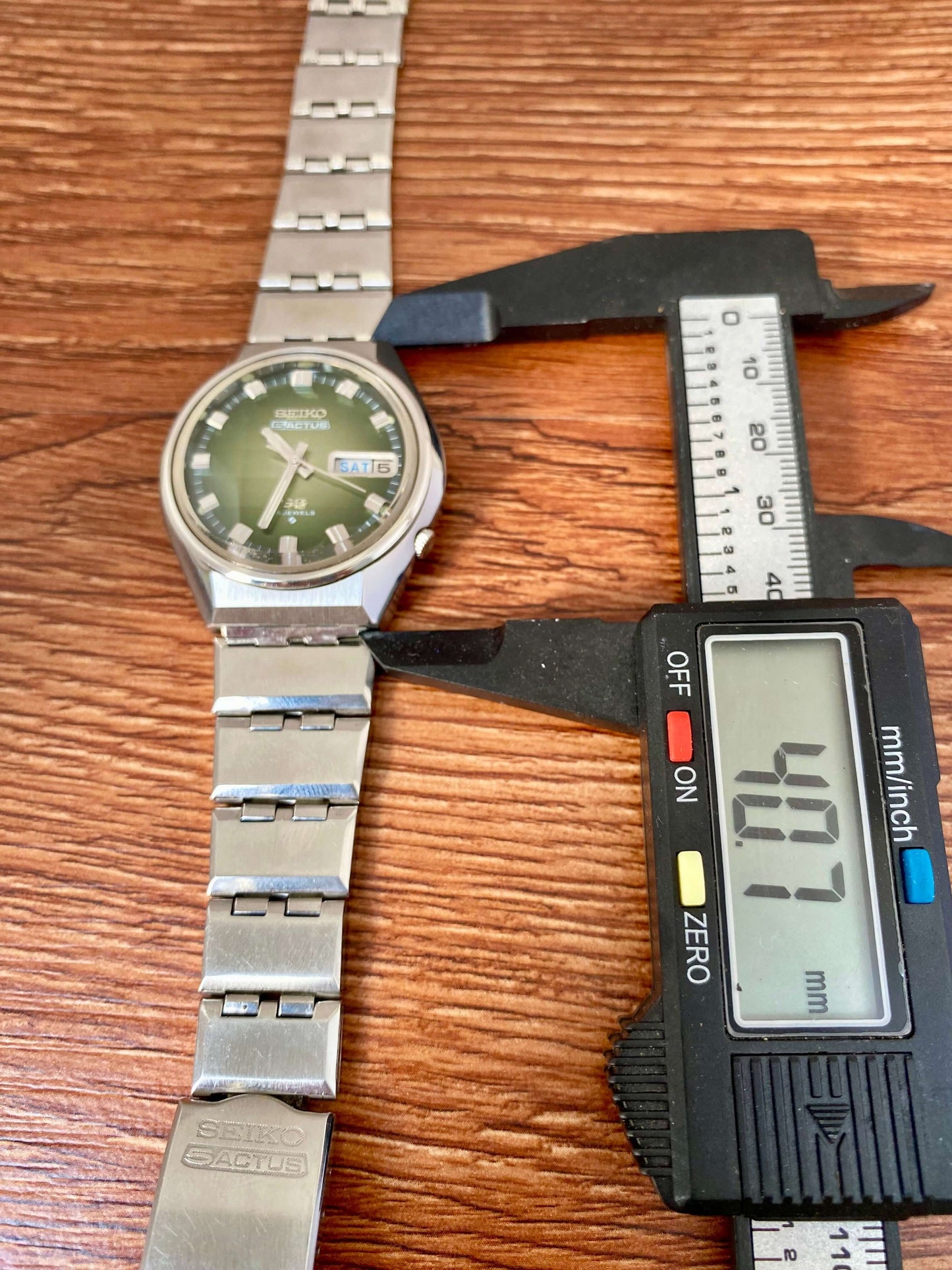 Vintage Seiko 5 Actus 6106-7690 on a wooden surface with calipers measuring its width in millimeters.