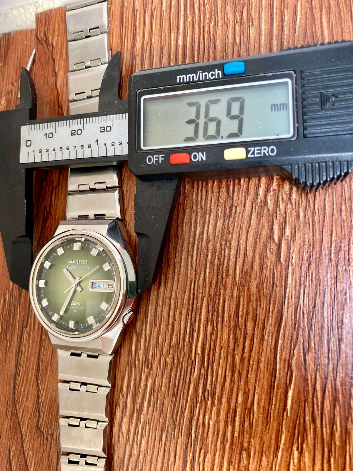 Vintage Seiko 5 Actus 6106-7690 displayed with caliper measuring 36.9 mm on wooden background.