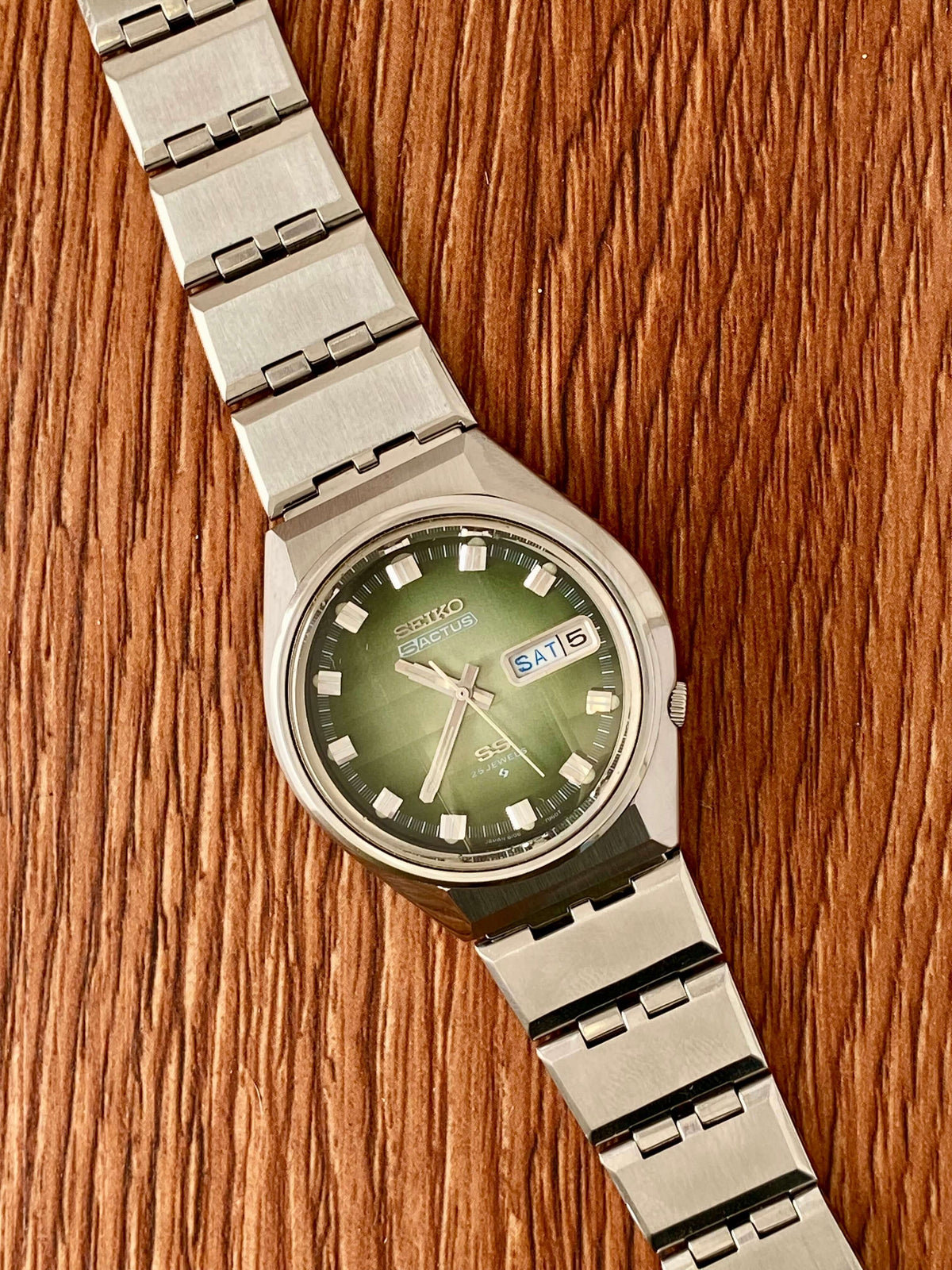 Vintage Seiko 5 Actus 6106-7690 with original green dial and stainless steel bracelet on wooden surface