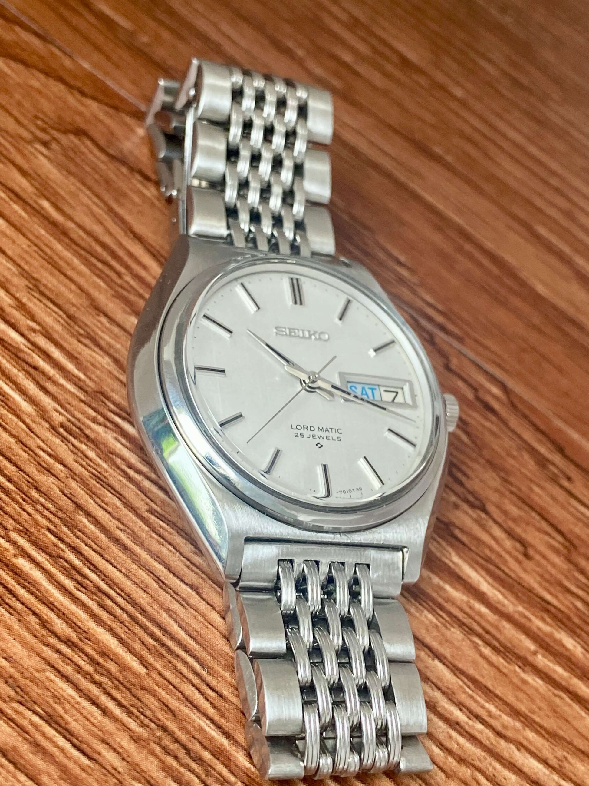 Vintage Seiko Lord Matic 5606-7010 on a woven steel bracelet, showcasing original white linen dial and date function.
