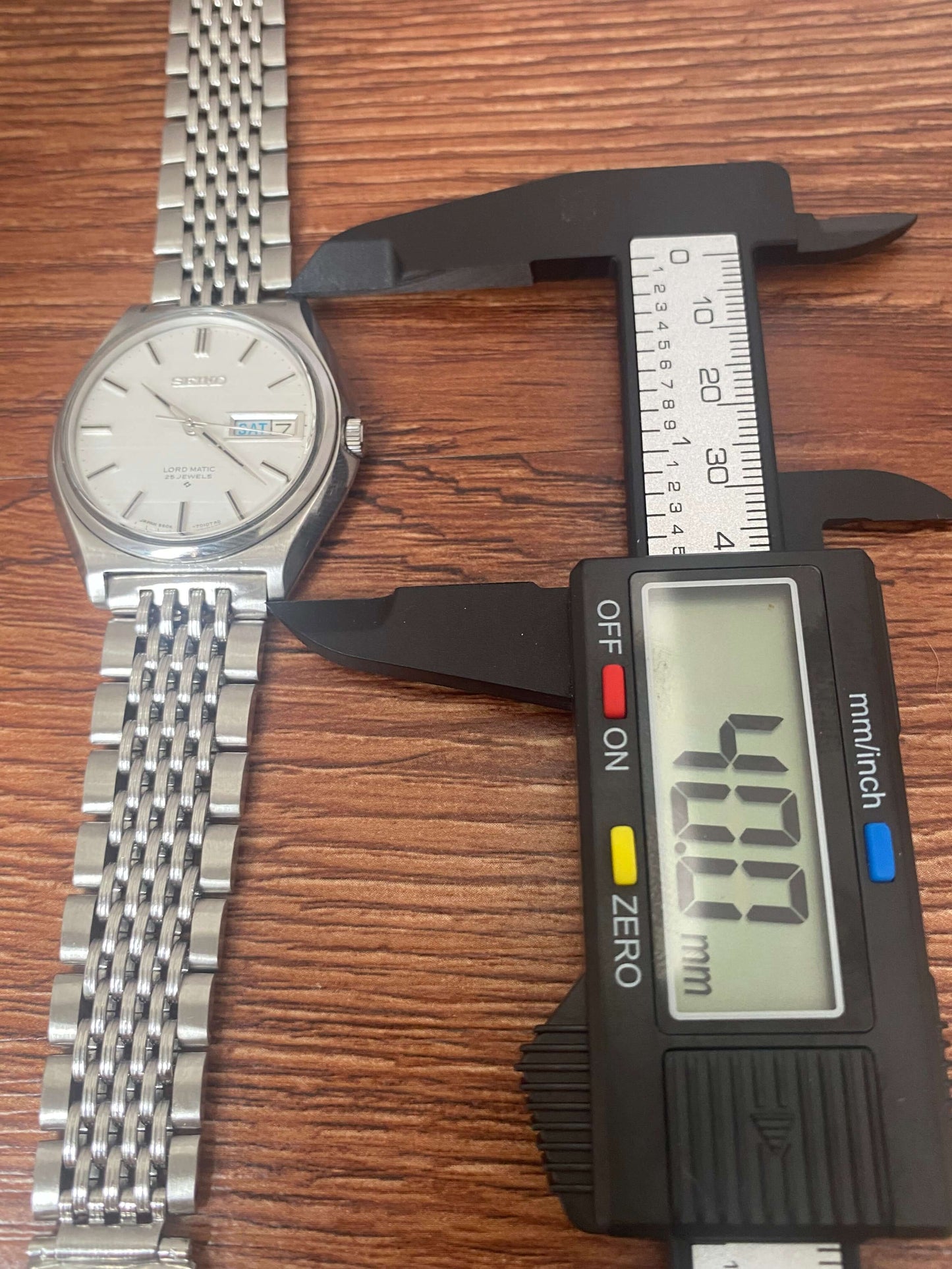Vintage Seiko Lord Matic 5606-7010 being measured for precision with calipers on wooden surface.