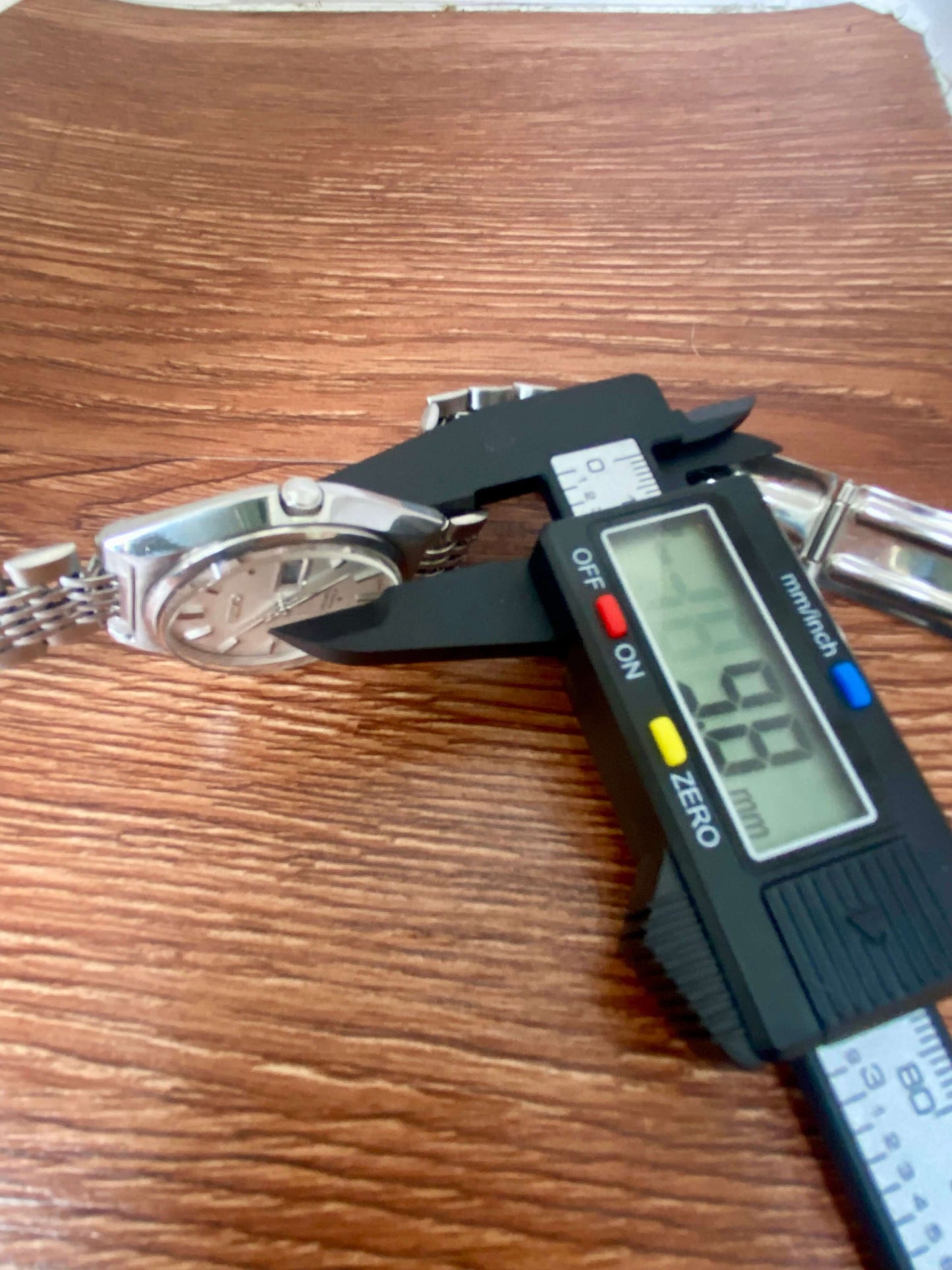 Vintage Seiko Lord Matic 5606-7010 being measured with calipers on a wooden surface.