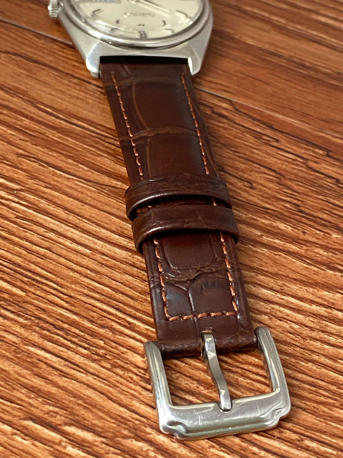 Vintage Seiko Lord Matic 5606-7000 brown leather strap with polished silver buckle on wooden surface.