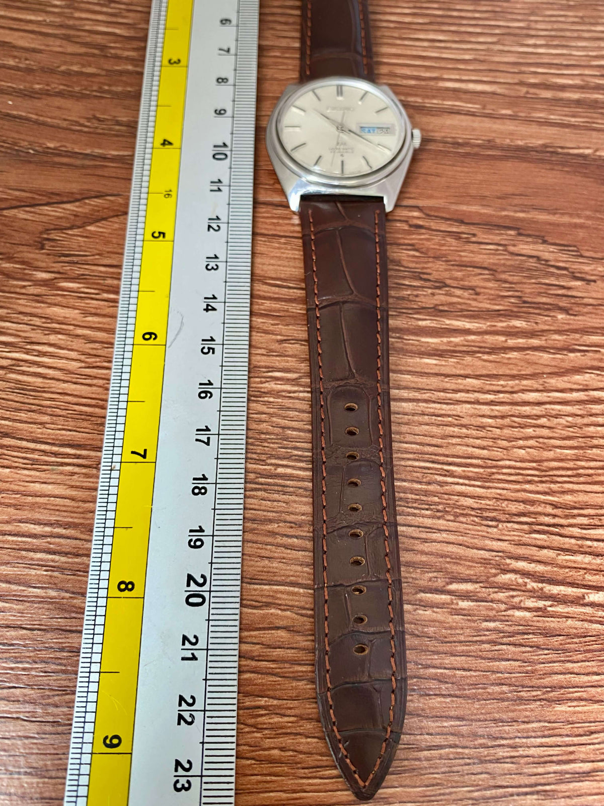 Vintage Seiko Lord Matic 5606-7000 watch with a brown leather strap and ruler for size comparison.